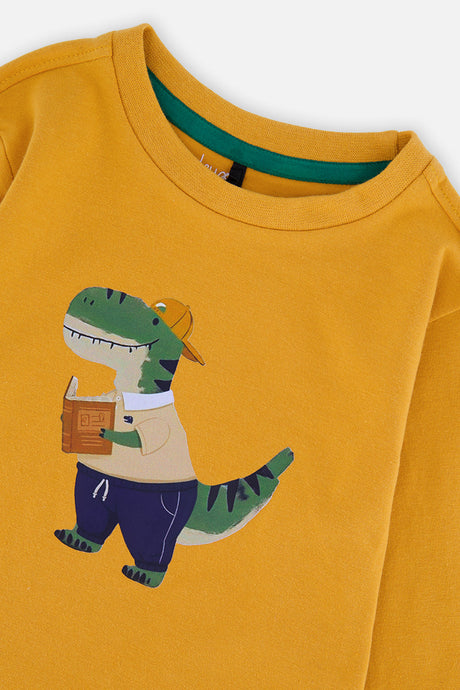 Close-up of the dinosaur graphic and deep green trim inside the neckline of the mustard yellow tee