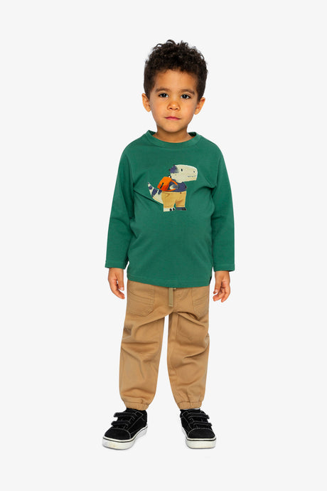 Child wearing the green dinosaur tee with tan jogger pants and black sneakers, full-length view