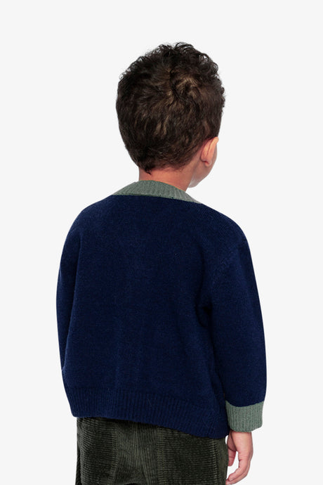 Back view of a child wearing the Deux par Deux navy knit cardigan with green neck trim