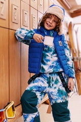 Child leaning on a wooden locker wall in the blue mountain print fleece pullover under a blue vest, holding a mug