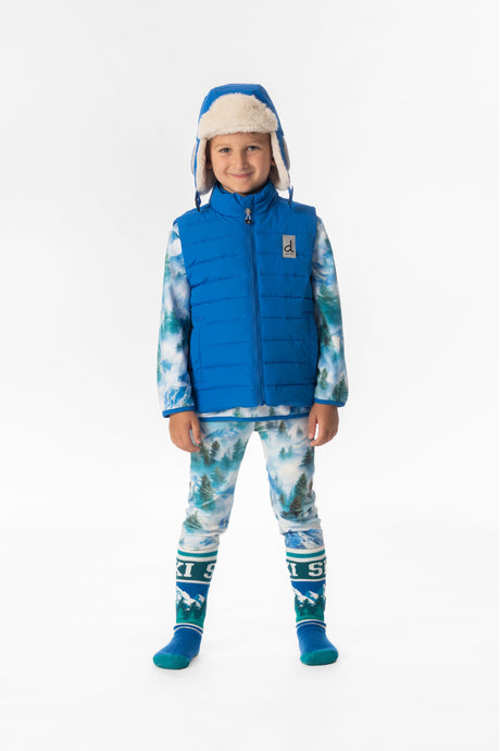 Boy standing in the blue Deux par Deux quilted vest over a forest print base layer, full-length front view