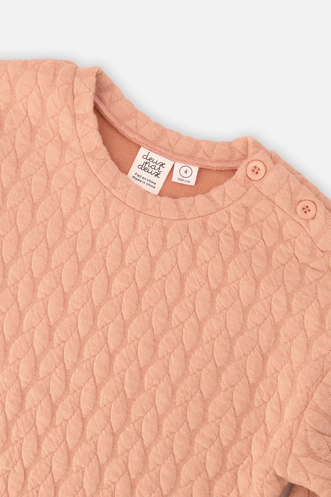 Close-up of the quilted pattern and shoulder buttons on the peach-pink Deux par Deux sweatshirt