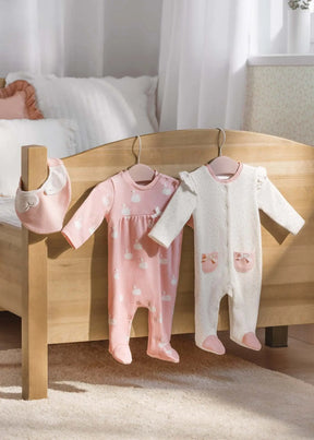 Two swan-print baby sleepsuits and pink bib displayed by wooden crib