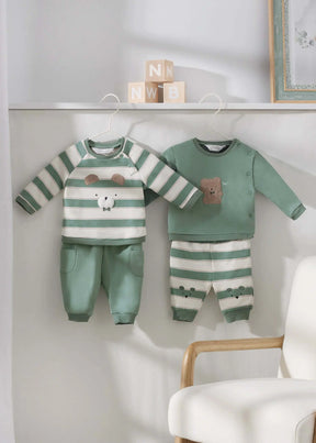 Two sage and ivory baby outfits with bear details hanging in nursery