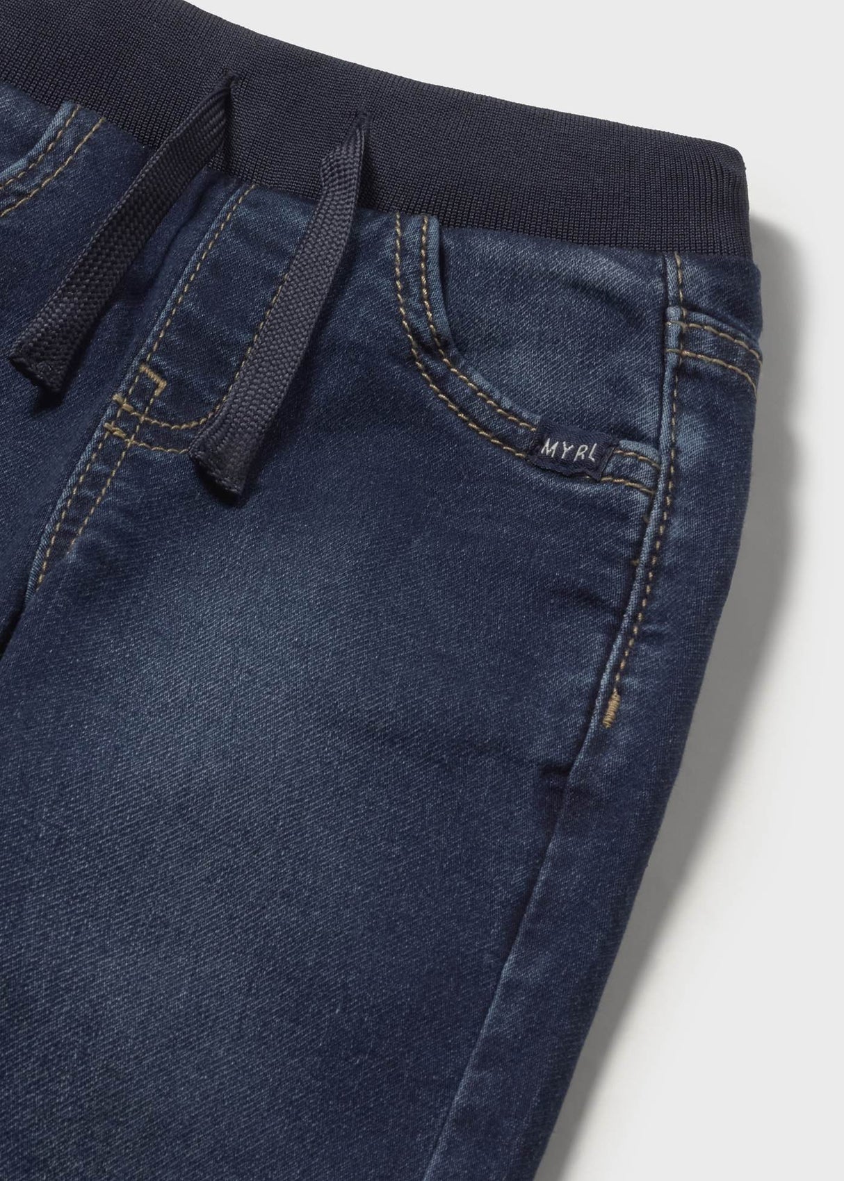 Closeup of elastic waistband and adjustable drawstring on kids denim pants.