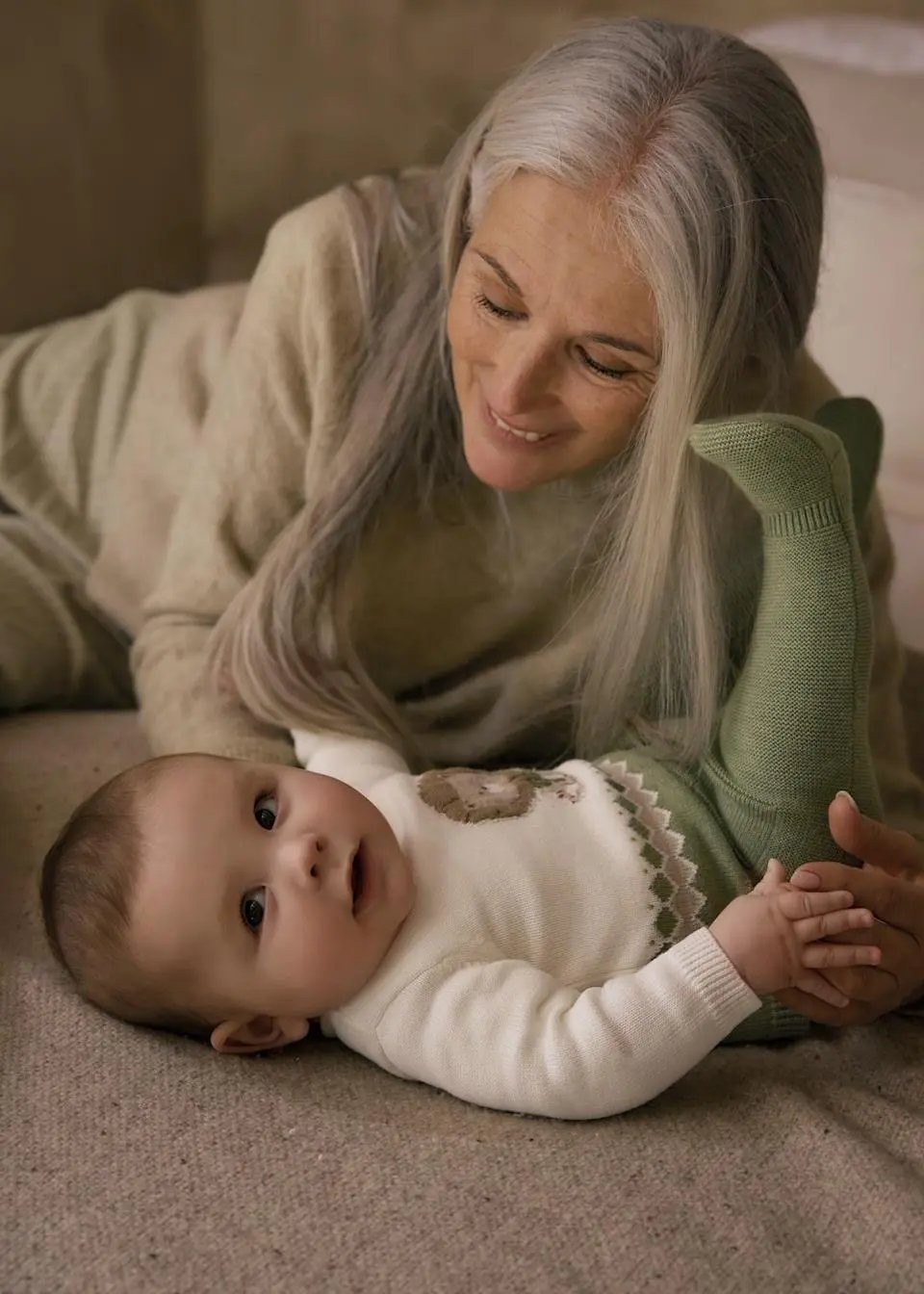Lifestyle image of newborn wearing ivory knit sweatshirt and olive pants, cozy at home.