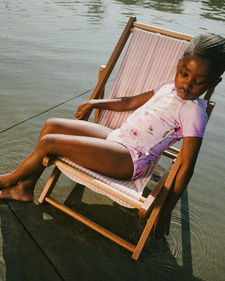Girl relaxing on dock chair wearing purple flower print one-piece swimsuit