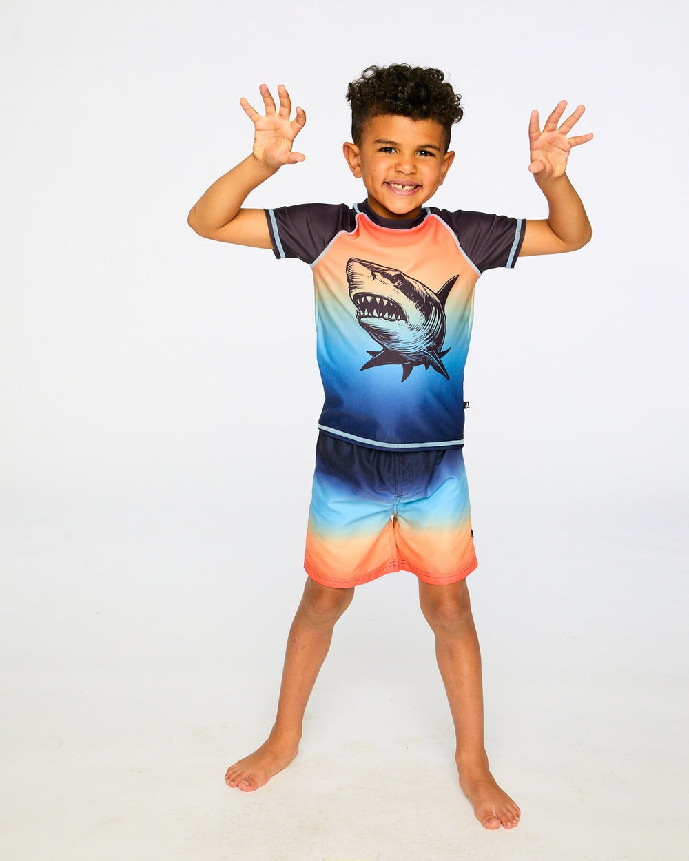 Boy standing in studio posing in shark graphic rashguard swim shirt front view