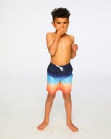 Boy standing in studio in blue/orange gradient swim trunks front view