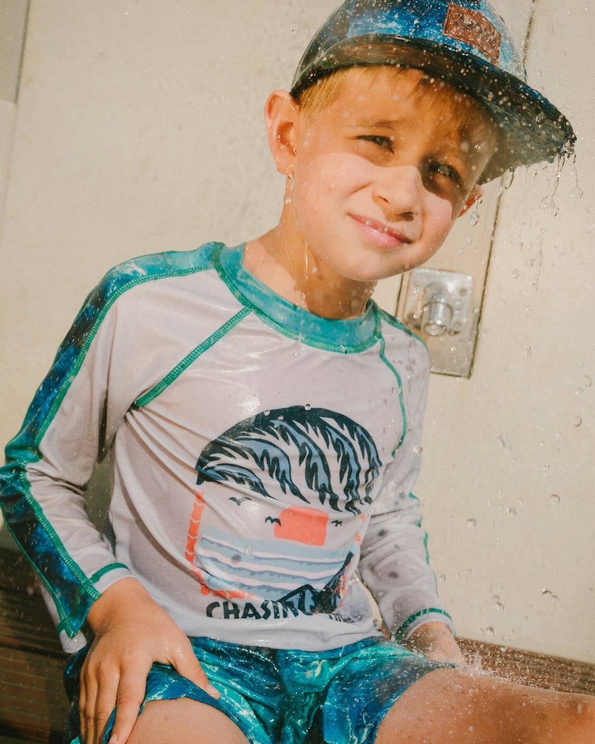Boy sitting in blue rashguard and blue waves boys swim trunks front view