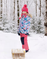 Girl wearing flash-coral jacket and snow pants with detachable hood and snow skirt.