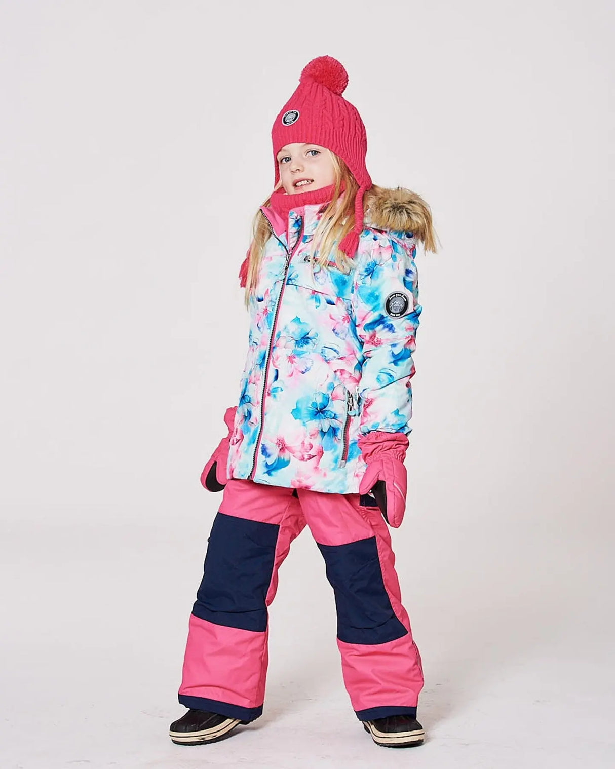 Girl in flash-coral print jacket and navy pants standing in snow, grow sleeves visible.