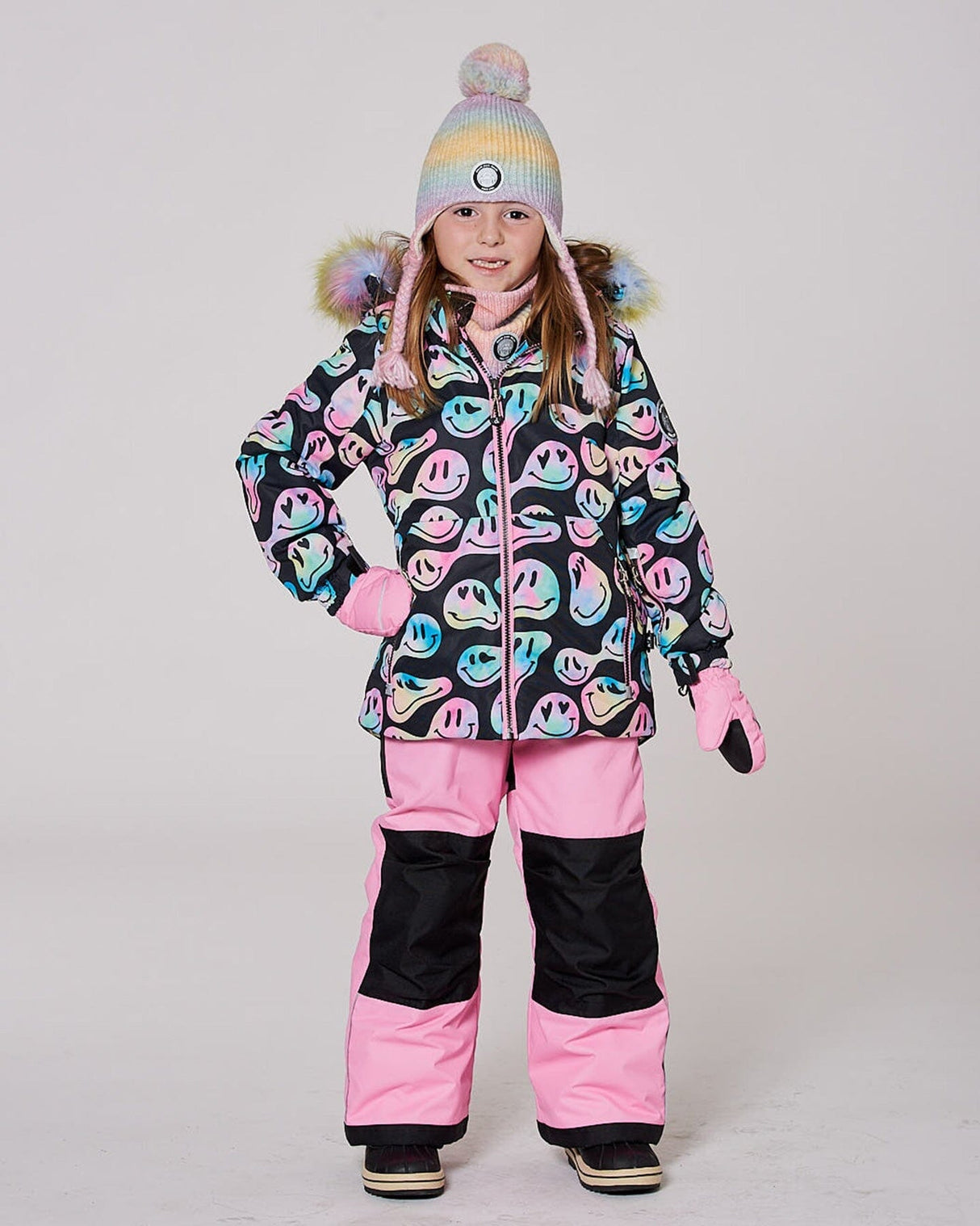 Model in two-piece ski suit pink bib pants, smiley jacket hood up — almost gone