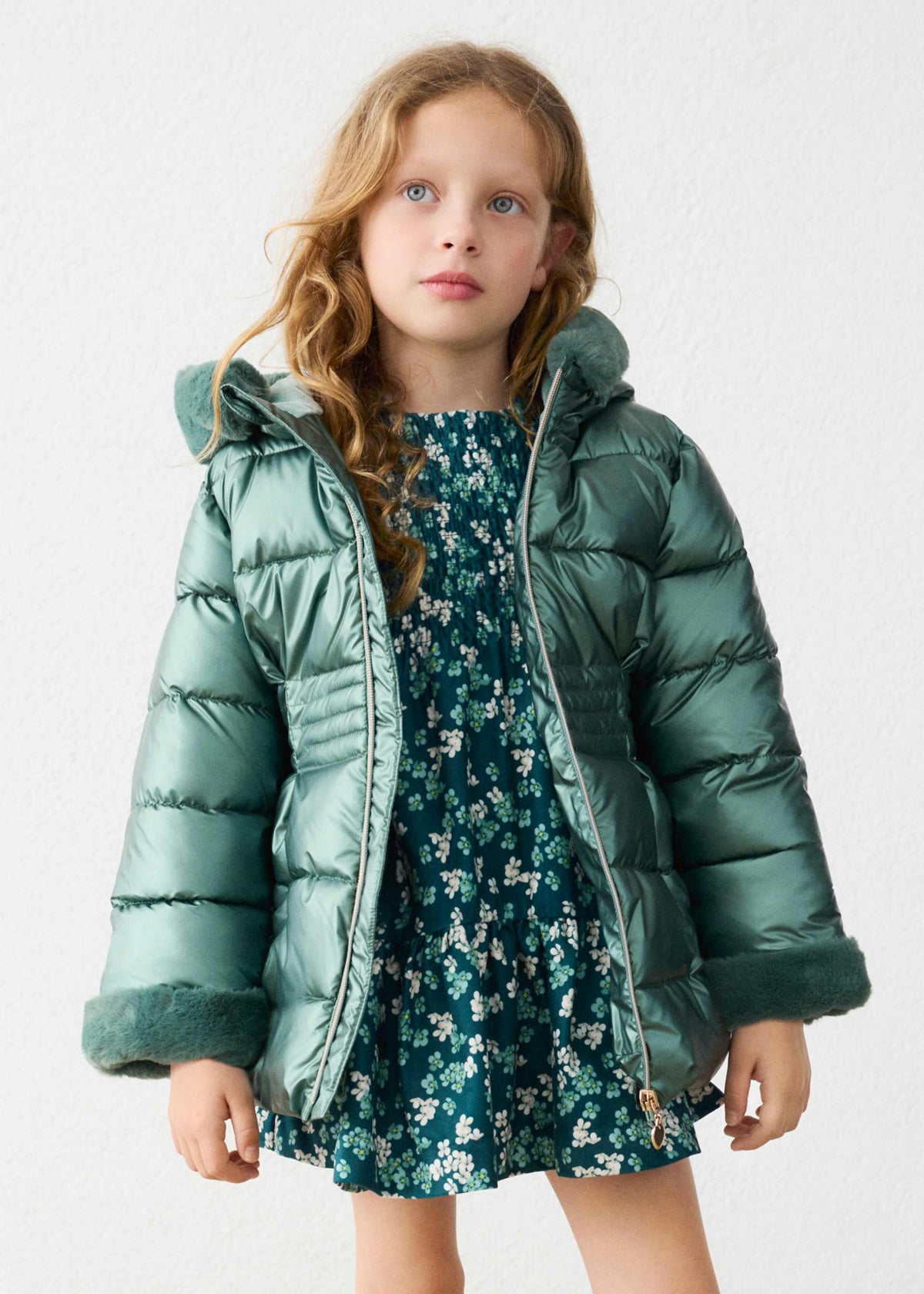 Girl in a floral dress wearing the shiny green puffer coat open at the front