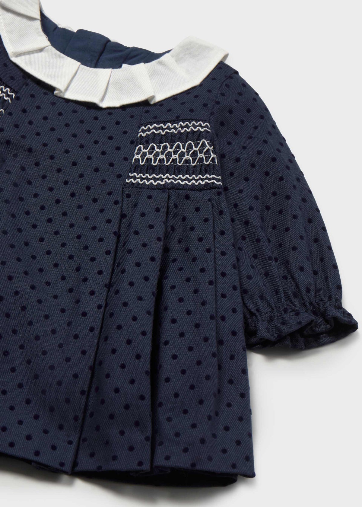 Close-up of the white-stitched smocking, pleated ivory collar and ruffled cuff on the navy dotted dress