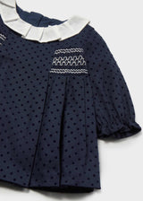 Close-up of the white-stitched smocking, pleated ivory collar and ruffled cuff on the navy dotted dress