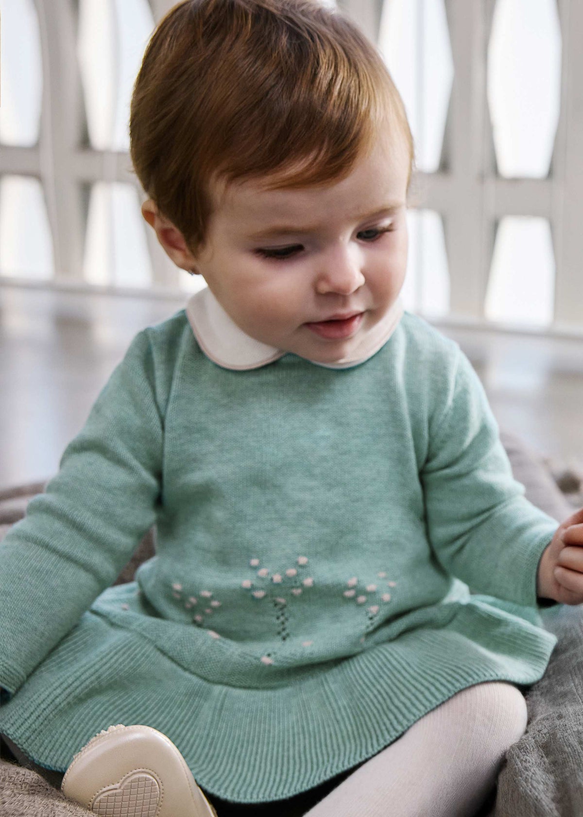 Baby wearing the sage green knit dress with cream Peter Pan collar